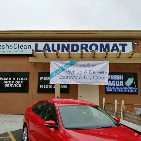 Laundromat in San Diego & Chula Vista - Close-up of a person holding a white plastic hamper filled with laundry in front of laundromat washing machines