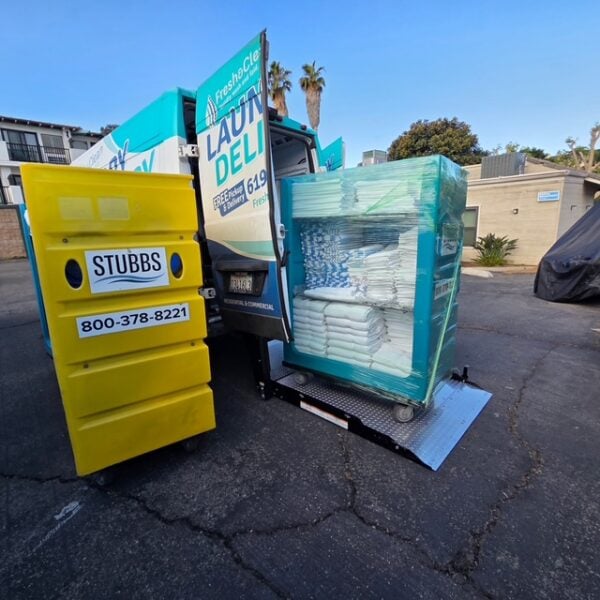 Laundromat in San Diego & Chula Vista - Close-up of a person holding a white plastic hamper filled with laundry in front of laundromat washing machines