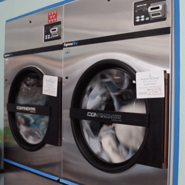 Laundromat in San Diego & Chula Vista - Close-up of a person holding a white plastic hamper filled with laundry in front of laundromat washing machines