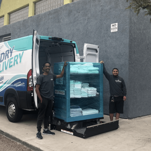 Laundromat in San Diego & Chula Vista - Close-up of a person holding a white plastic hamper filled with laundry in front of laundromat washing machines