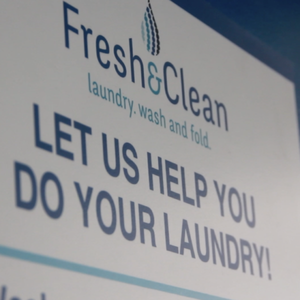 Laundromat in San Diego & Chula Vista - Close-up of a person holding a white plastic hamper filled with laundry in front of laundromat washing machines