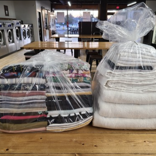 Laundromat in San Diego & Chula Vista - Close-up of a person holding a white plastic hamper filled with laundry in front of laundromat washing machines