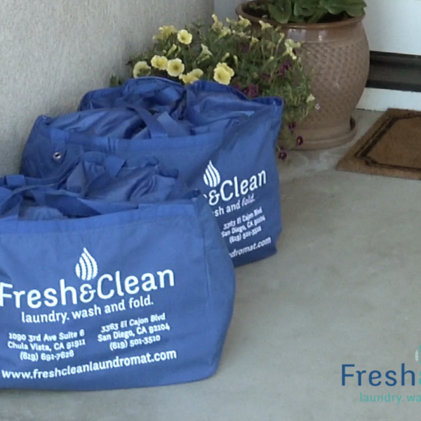 Laundromat in San Diego & Chula Vista - Close-up of a person holding a white plastic hamper filled with laundry in front of laundromat washing machines
