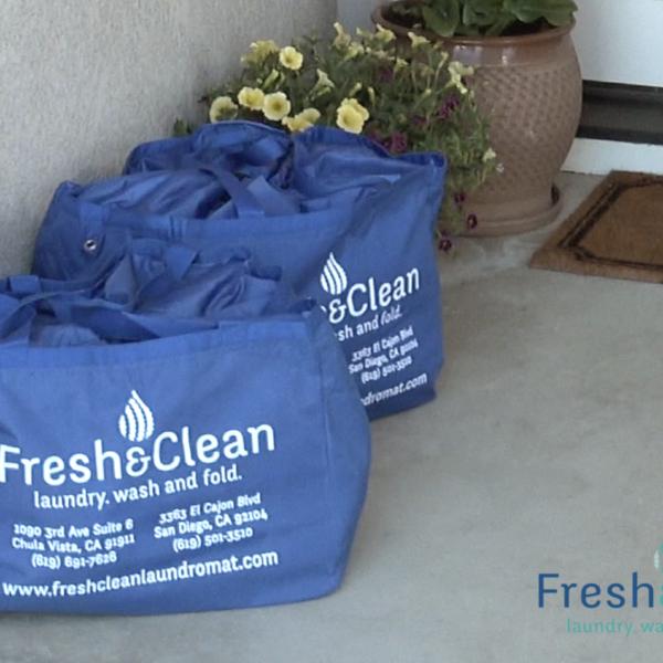 Laundromat in San Diego & Chula Vista - Close-up of a person holding a white plastic hamper filled with laundry in front of laundromat washing machines