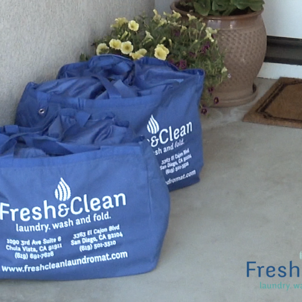 Laundromat in San Diego & Chula Vista - Close-up of a person holding a white plastic hamper filled with laundry in front of laundromat washing machines