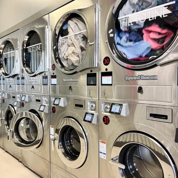 Laundromat in San Diego & Chula Vista - Close-up of a person holding a white plastic hamper filled with laundry in front of laundromat washing machines