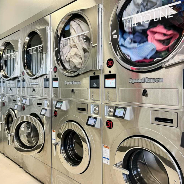 Laundromat in San Diego & Chula Vista - Close-up of a person holding a white plastic hamper filled with laundry in front of laundromat washing machines