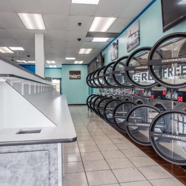 Laundromat in San Diego & Chula Vista - Close-up of a person holding a white plastic hamper filled with laundry in front of laundromat washing machines